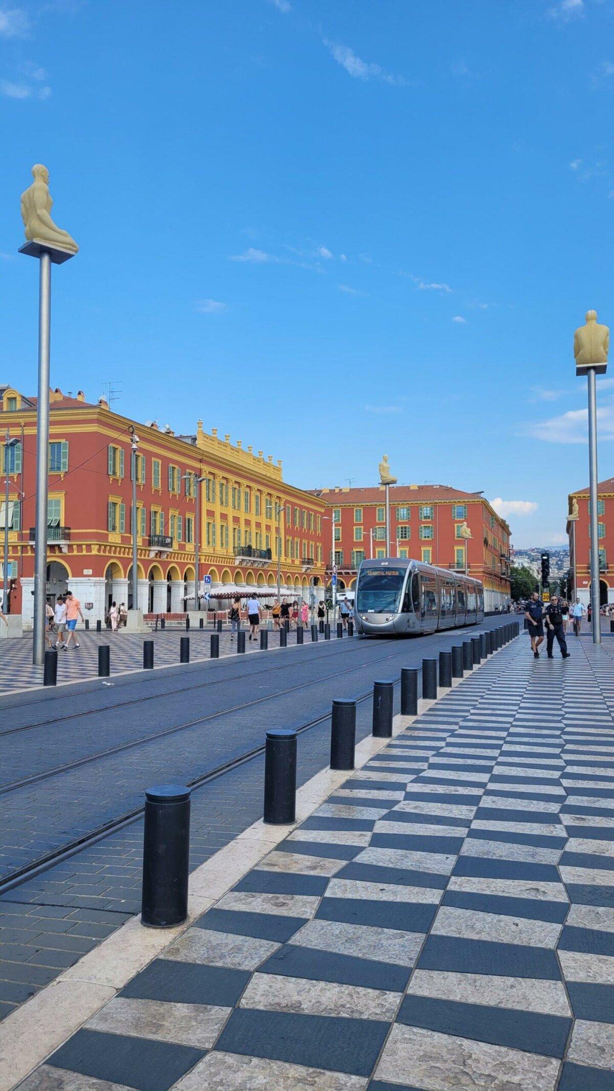Tranvía y tablero de ajedrez blanco y negro en la plaza Masséna en Niza, fachadas rojas y cielo azul