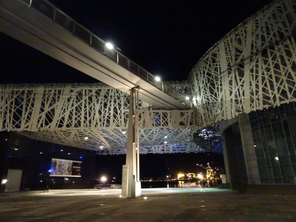 Mémorial ACTe de nuit : passerelle et résille métallique dominant le quai