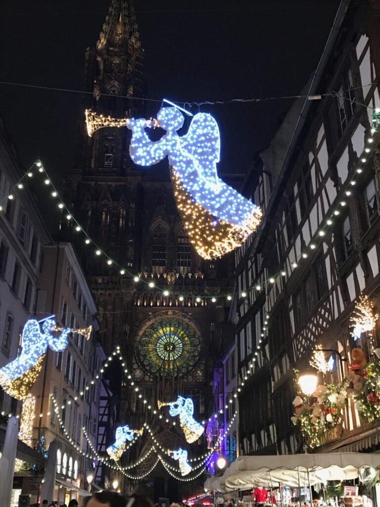 Illuminations de Noël en forme d’anges dans la rue Mercière à Strasbourg, avec la cathédrale en arrière-plan pendant les marchés de Noël