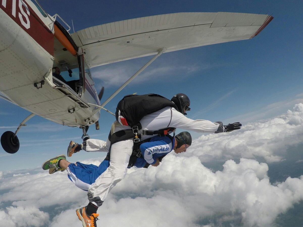 Tandem parachute jump exiting the plane above the clouds