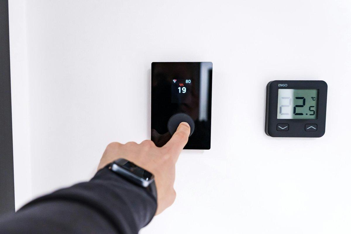 Main qui règle un thermostat mural numérique dans un logement
